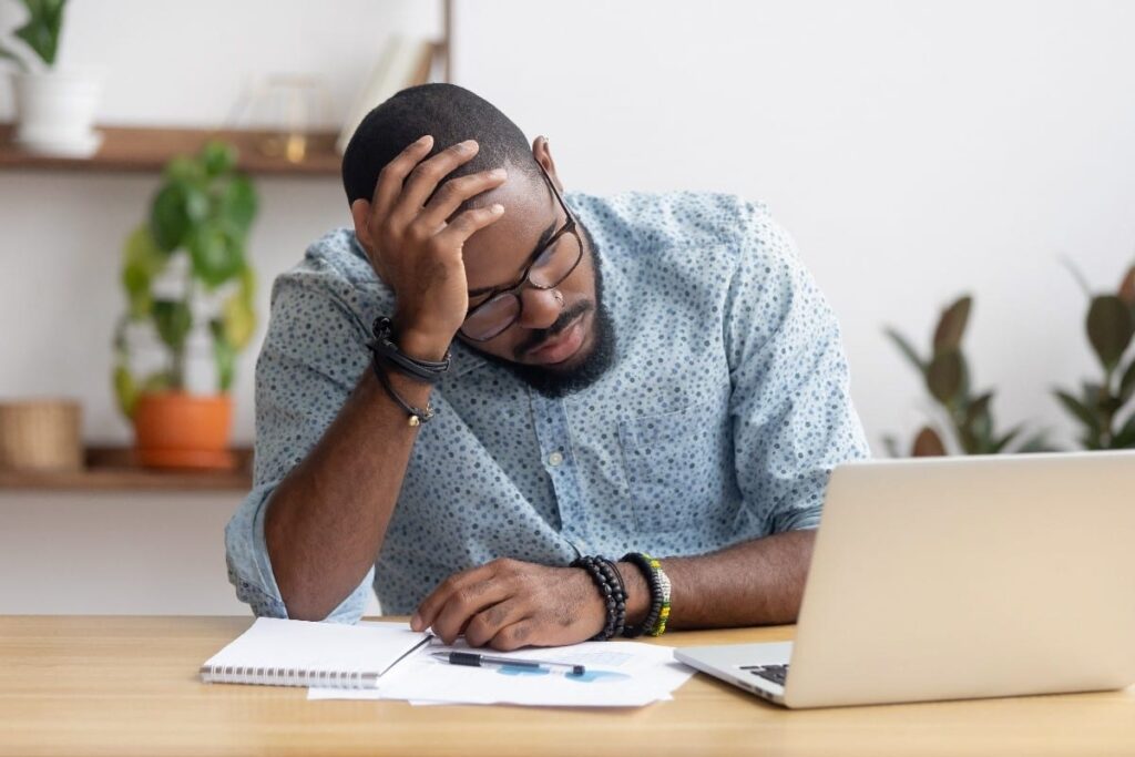 Stressed man at laptop with head in hand.